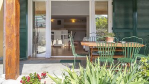 A patio area with a wooden table and chairs, a potted plant, and a view of the interior through open doors.