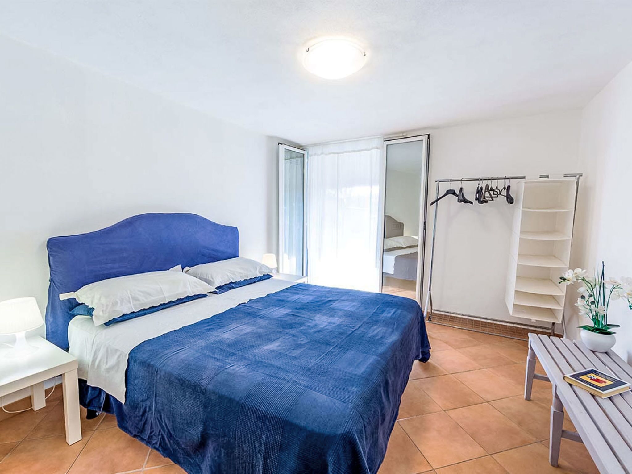 A bedroom with a bed, a bedside table, a chair, a wardrobe, and a small table with a book.