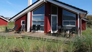 A red building with a large glass window and a white door, surrounded by tall grass. - Holiday Vital Resort (GBE111) by Interhome (Großenbrode)
