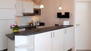 A modern kitchen with white cabinetry, a black countertop, a microwave, a coffee maker, and a toaster. There are two pendant lights hanging above the counter. - Holiday Vital Resort (GBE111) by Interhome (Großenbrode)