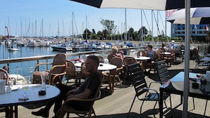 An outdoor seating area with tables and chairs, overlooking a marina with boats.
