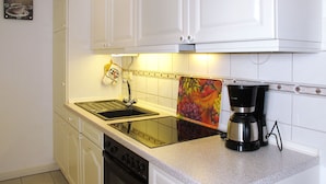 A kitchen with white cabinets, a black stove, a sink, and a coffee maker.