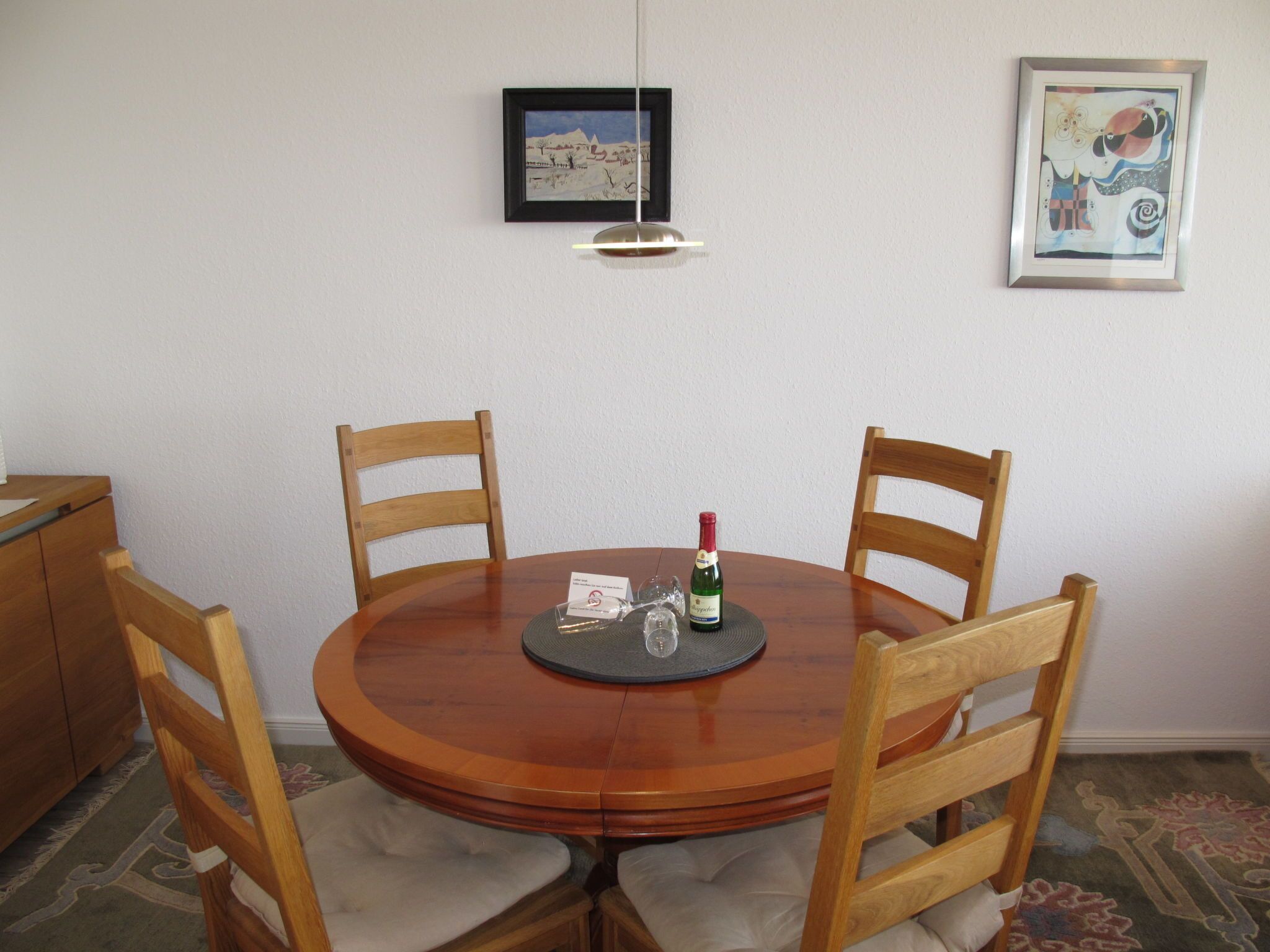 Een ronde houten eettafel met vier stoelen, een fles wijn en een menukaart op tafel.