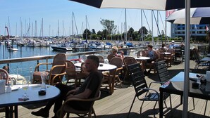 An outdoor seating area with tables and chairs, overlooking a marina with boats. - Ostsee-Residenz (DMP153) by Interhome (Damp)