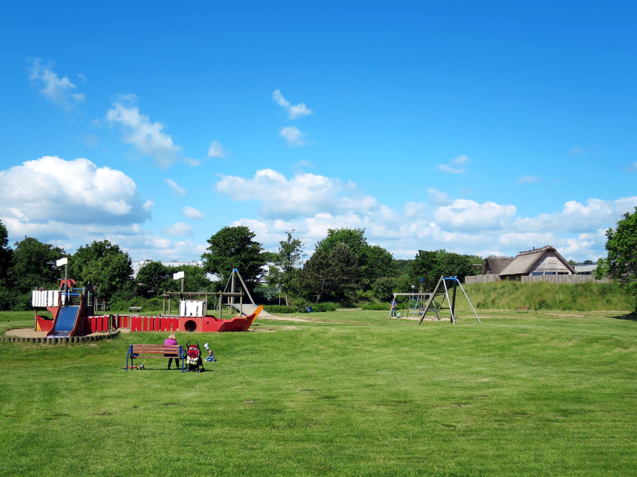 A playground with slides and swings, a bench, and a building in the background.