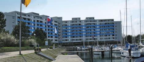 A marina with boats docked, a wooden dock, and a large building with blue and white stripes in the background.
