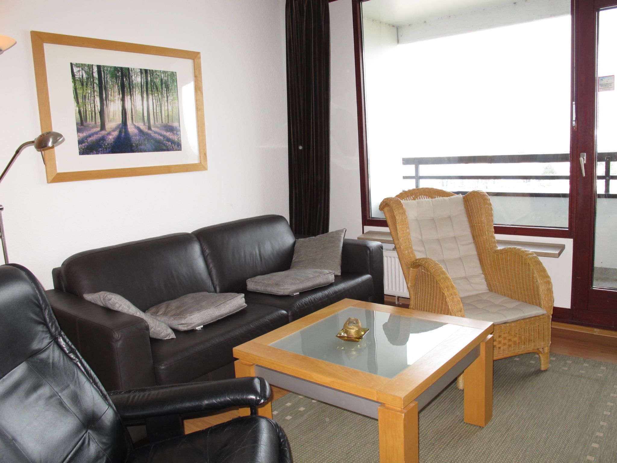 A living room with a black leather sofa, a glass-top coffee table, and a wicker armchair.