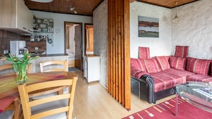 A cozy living room with a sofa, a glass coffee table, and a dining area with a wooden table and chairs. - Nordsee-Ferienhaus by Interhome (Friedrichskoog)