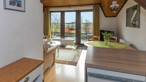 Una cocina con techo de madera, una zona de comedor con mesa y sillas, y vistas al exterior a través de amplios ventanales.