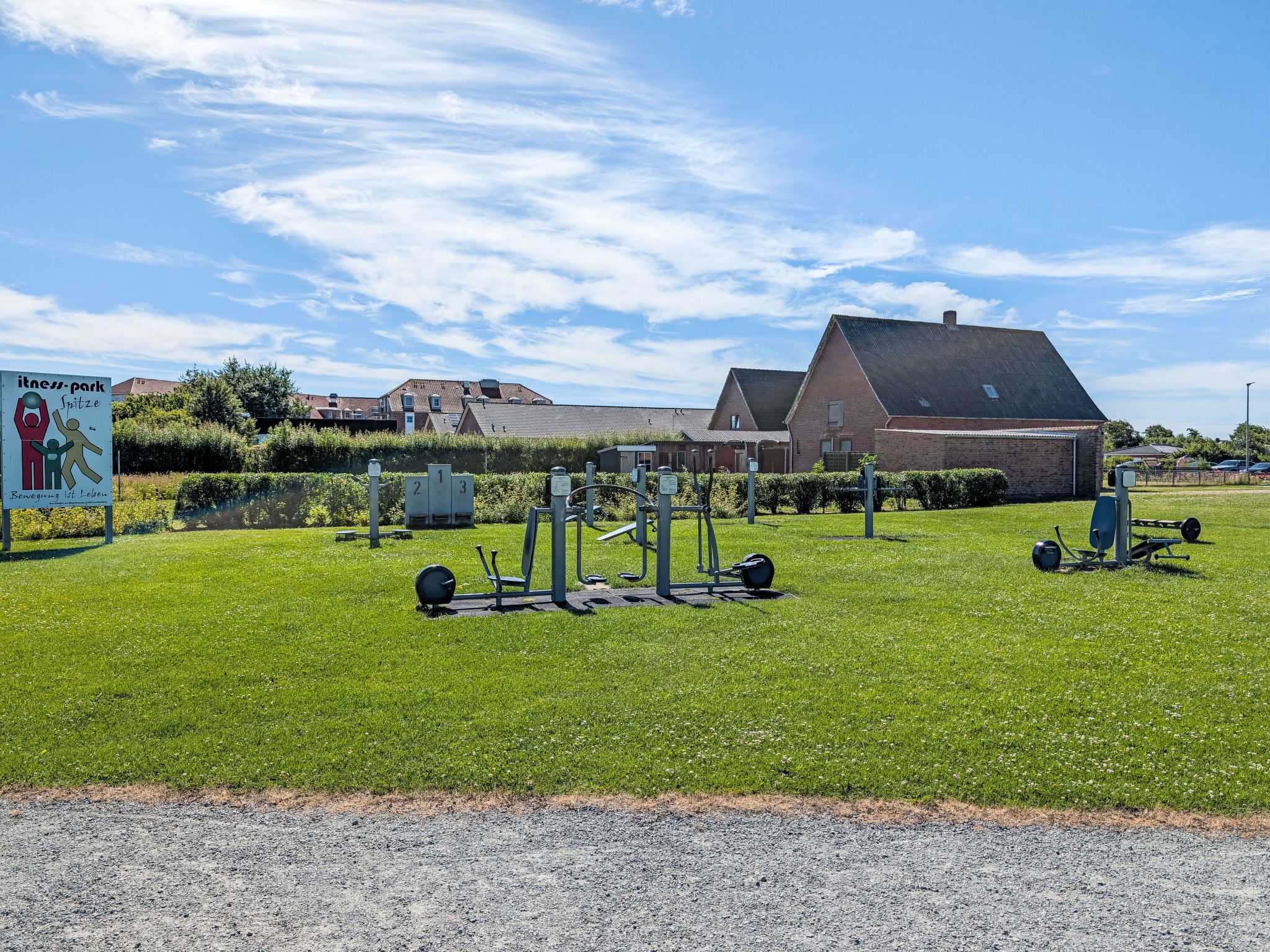 An outdoor fitness park with exercise equipment, a signboard, and a building in the background.