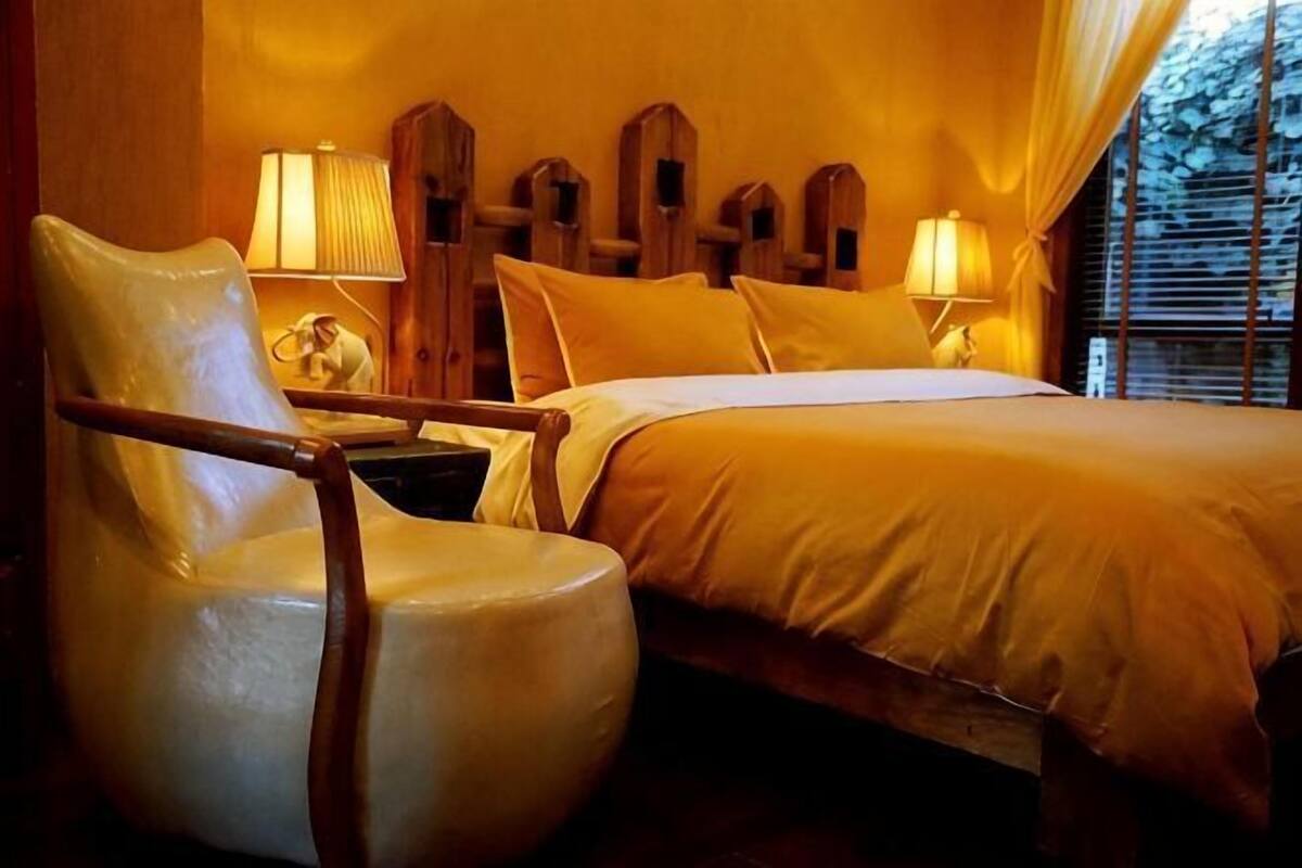 A hotel room with a bed, a chair, two lamps, and a window with curtains.