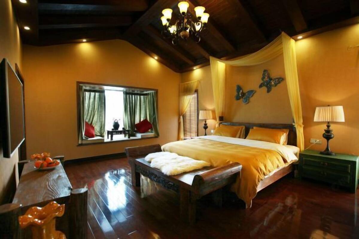 A bedroom with a large bed, a wooden bench, a mirror, and a chandelier.