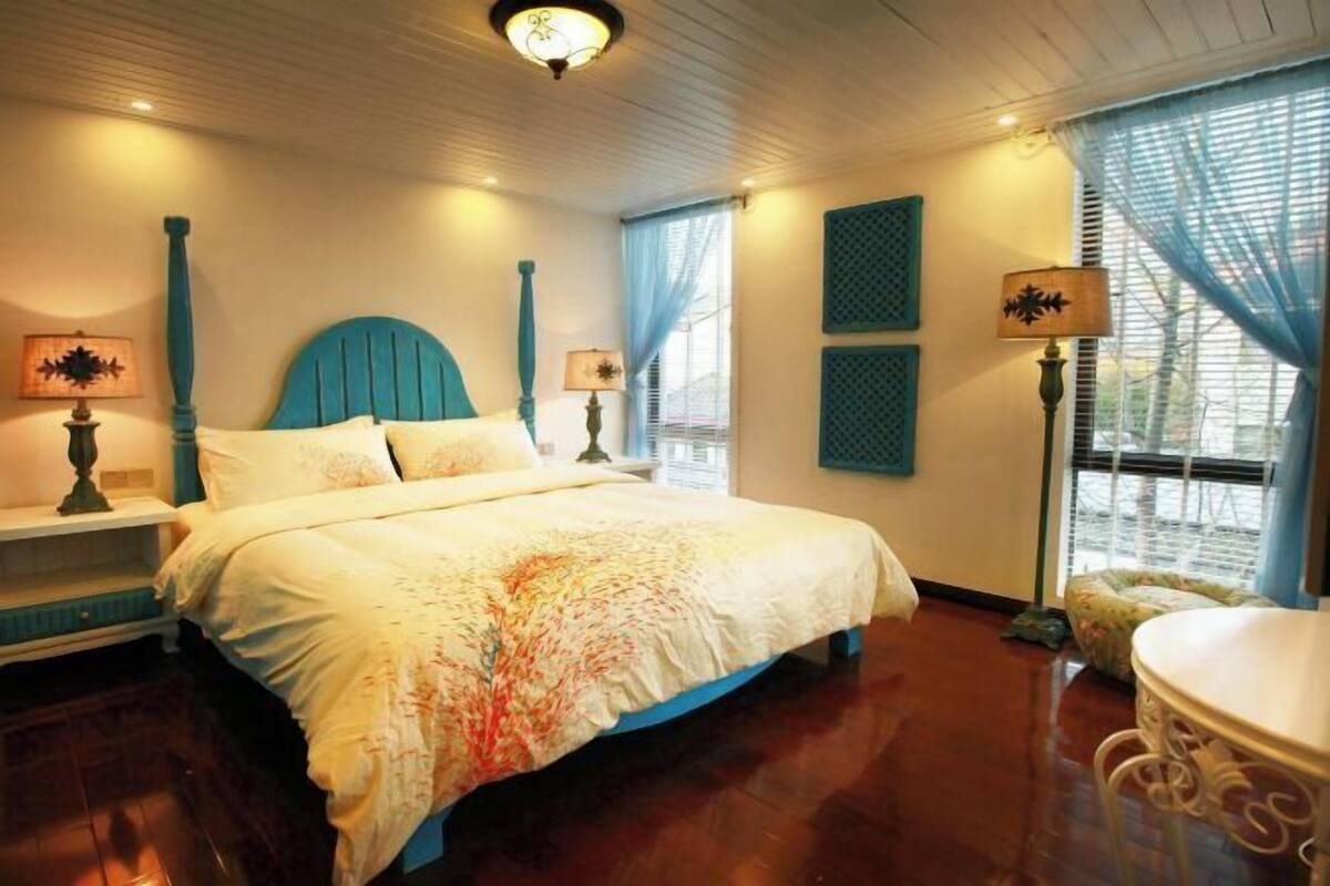 A bedroom with a bed, two bedside tables, a window with curtains, and a round table.