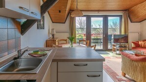 Eine moderne Küche mit Holzbalkendecke, ein Essbereich mit Tisch und Stühlen sowie ein Wohnzimmer mit Sofa und Fernseher.