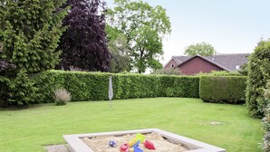 A rectangular sandbox with sand and toys, surrounded by a well-maintained lawn and hedges.