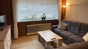 A cozy living room with a wooden ceiling, a sofa, a coffee table, and a TV on a wooden cabinet.