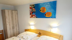 Ein Schlafzimmer mit einem Holz-Kopfteil, blumigem Bettbezug, zwei Nachttischlampen und einem Wandbild von Fischen.