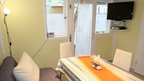 A room with a bed, a table with a striped tablecloth, a TV on a stand, and a window with curtains. - Osterende by Interhome (Otterndorf)