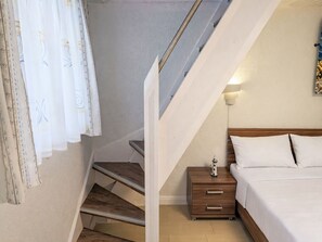 Ein Schlafzimmer mit einem hölzernen Bett, einem Nachttisch, einer Lampe und einer Treppe, die zu einem Erkerbereich führt.