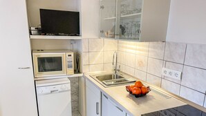 Uma cozinha moderna com micro-ondas embutido, máquina de lavar loiça, uma pia e uma tigela de laranjas na bancada.