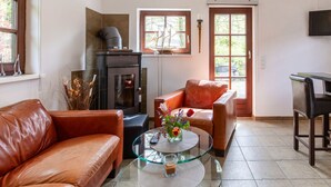 Una sala de estar con chimenea, sofá de cuero, mesa de centro de vidrio y televisor montado en la pared.