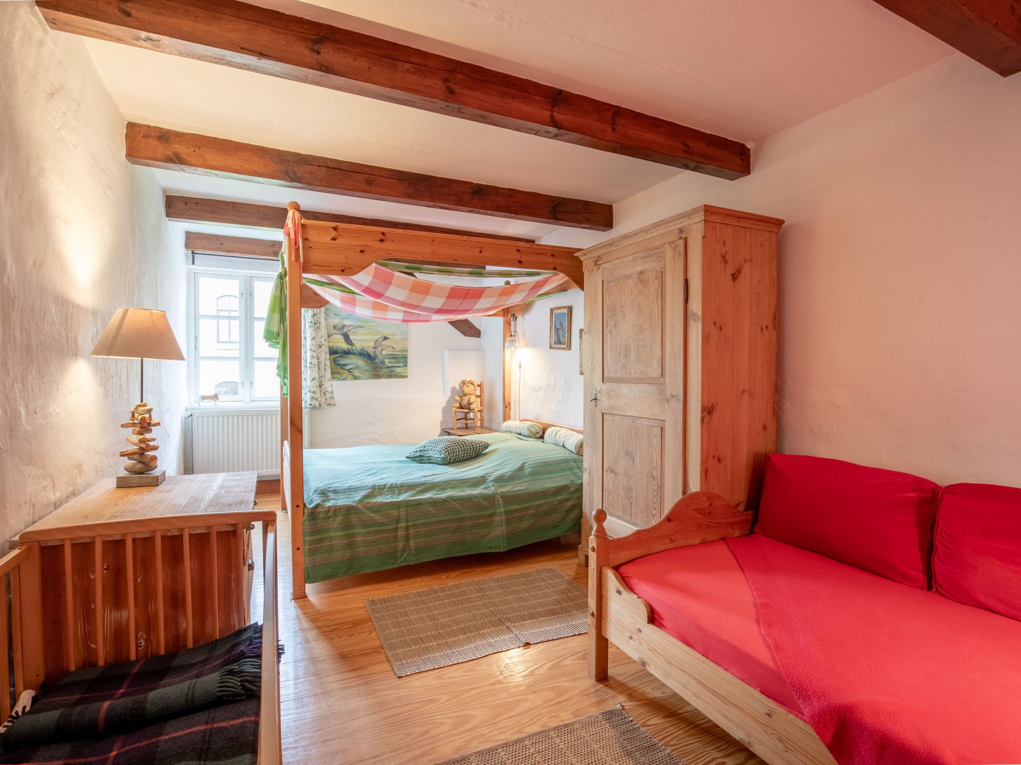 A cozy bedroom with a wooden bed, a red sofa, a wooden nightstand, and a lamp.