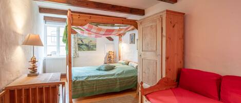 A cozy bedroom with a wooden bed, a red sofa, a wooden nightstand, and a lamp.