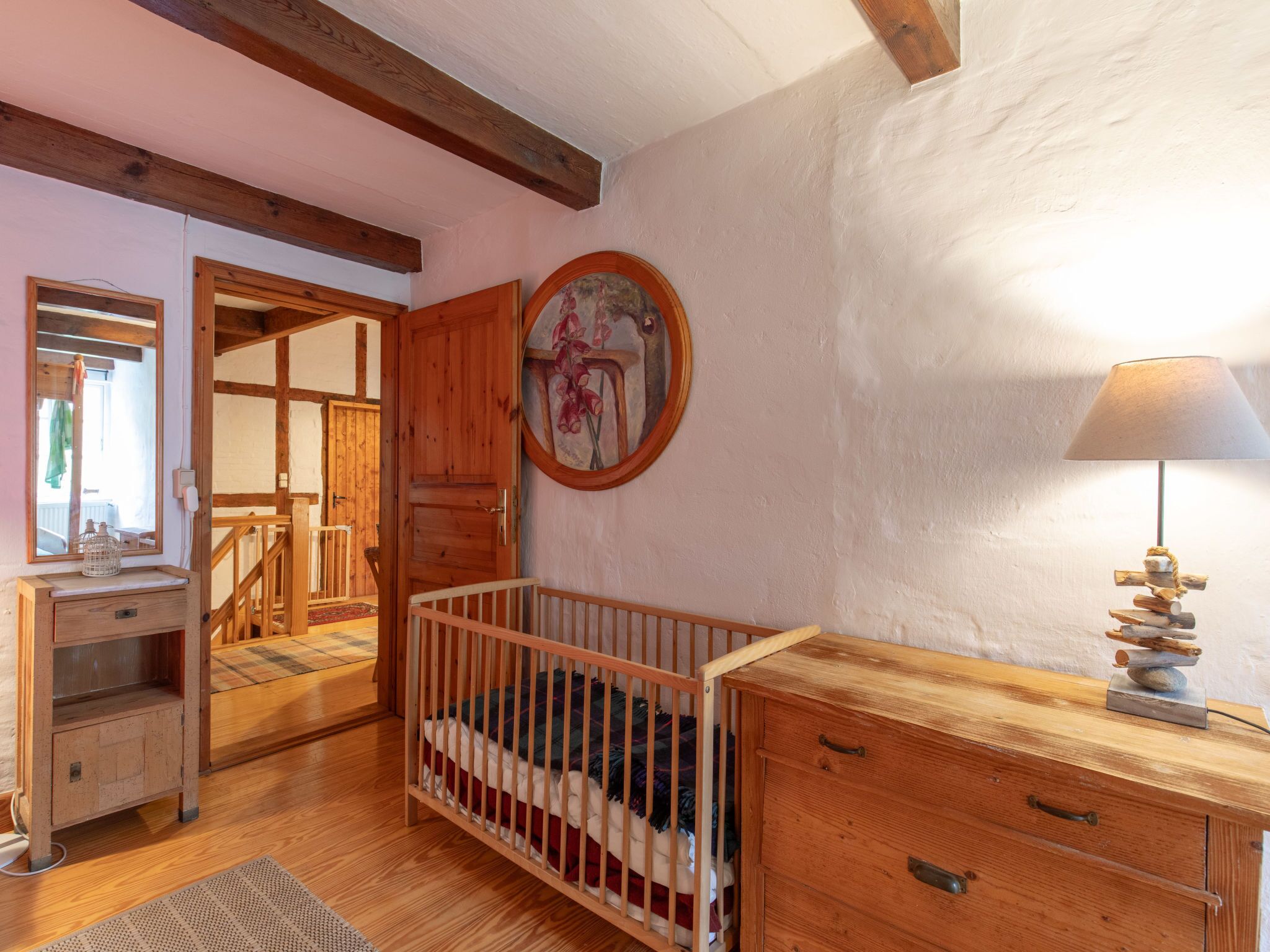 A cozy room with a wooden crib, a dresser, a mirror, and a lamp.
