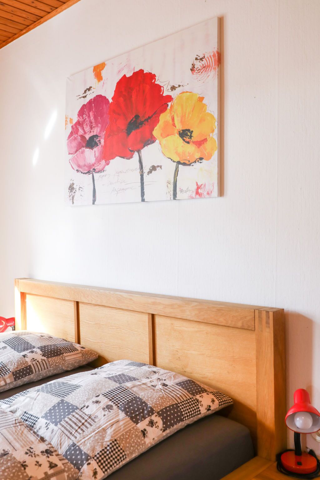 Una camera da letto con una testiera in legno, un letto con biancheria a motivi decorativi e un quadro di fiori appeso al muro.