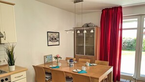 A dining area with a wooden table, chairs, a cabinet, and a window with red curtains. - Boddenzauber by Interhome (Breege)