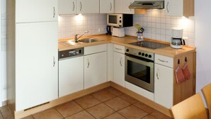 A kitchen with white cabinets, a dishwasher, an oven, a microwave, and a coffee maker. - Boddenzauber by Interhome (Breege)