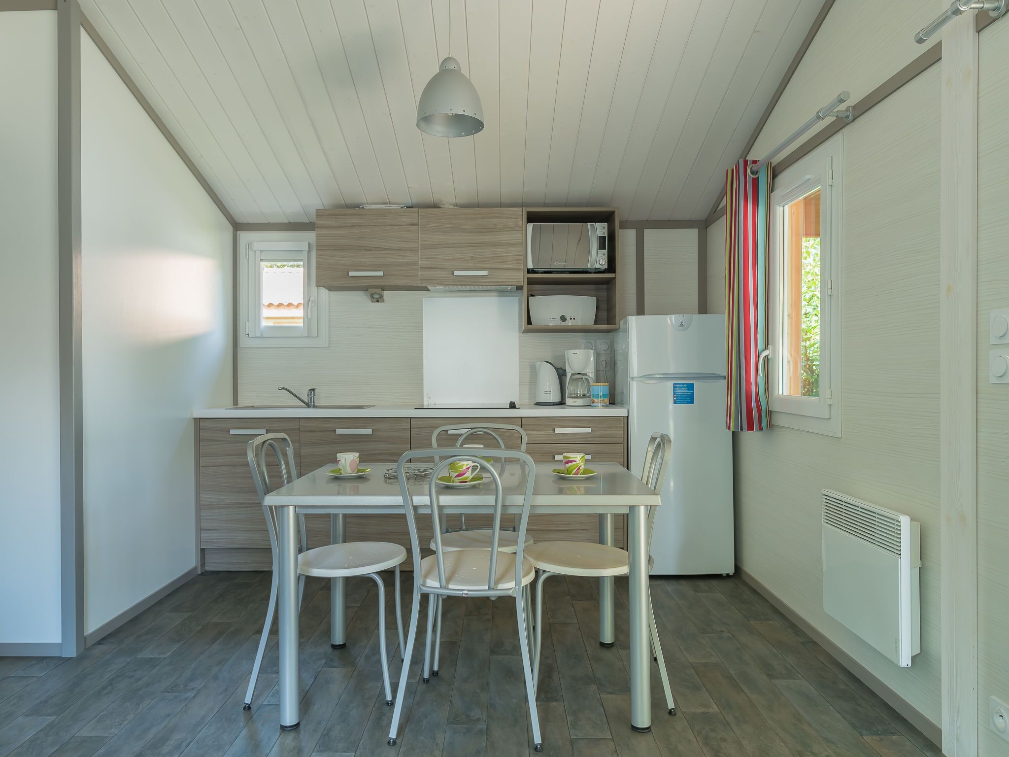 A modern kitchen with a dining table and chairs, a refrigerator, and a window with curtains.