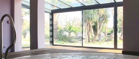 A spa room with a hot tub, large windows, and a view of the outdoors.