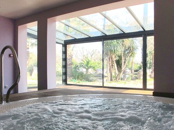 A spa room with a hot tub, large windows, and a view of the outdoors.