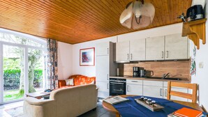 A cozy living area with a sofa, a dining table with chairs, a kitchen with cabinets and appliances, and a large window with a view of greenery. - von Dollen by Interhome (Wingst)