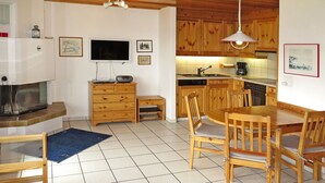 A cozy living room with a fireplace, wooden furniture, a TV, and a kitchen area with wooden cabinets and a dining table.