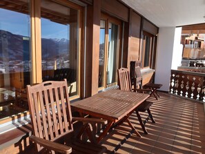 A wooden deck with a table and chairs, large windows with a mountain view, and a kitchen area. - BergSicht by Interhome (Laax)