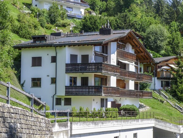 A multi-story building with balconies, a stone retaining wall, and a hillside backdrop. - BergSicht by Interhome (Laax)