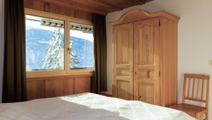 A bedroom with a large bed, wooden wardrobe, and a window with a view of snow-covered trees.