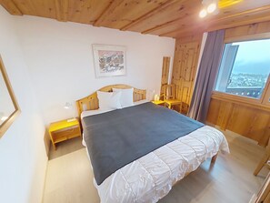 Quarto com cama, mesa de cabeceira, cadeira, janela com vista e um quadro na parede.