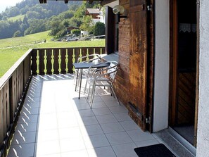 A balcony with a table and chairs, a wooden door, and a view of a green landscape. - Muotta Sulegl 4 by Interhome (Laax)