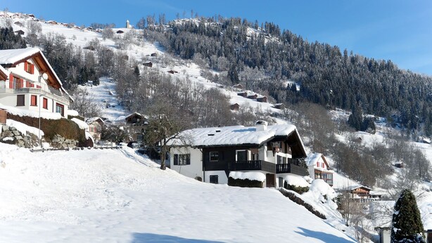 A snow-covered mountain village with traditional wooden houses, a clear blue sky, and a ski slope in the background. - Muotta Sulegl 4 by Interhome (Laax)