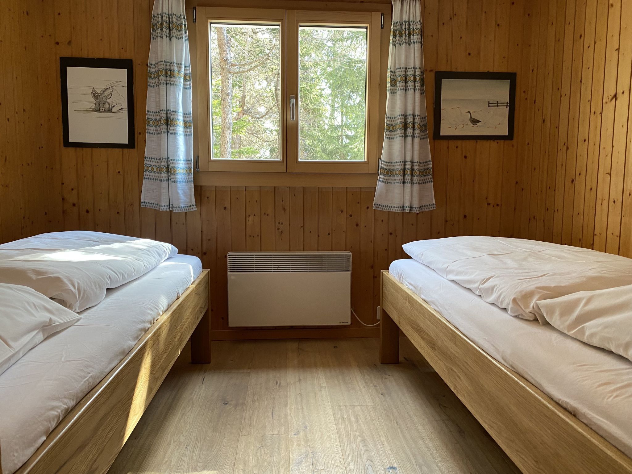 Una habitación con dos camas de madera, una ventana con cortinas e imágenes enmarcadas en las paredes.