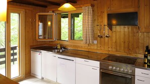 A kitchen with wooden cabinets, a stainless steel sink, a dishwasher, a stove, and a window with curtains. - Chalet Soldanella (BEL205) by Interhome (Bellwald)