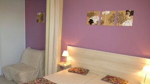 A bedroom with a bed, a nightstand, a lamp, a chair, and a window with curtains.