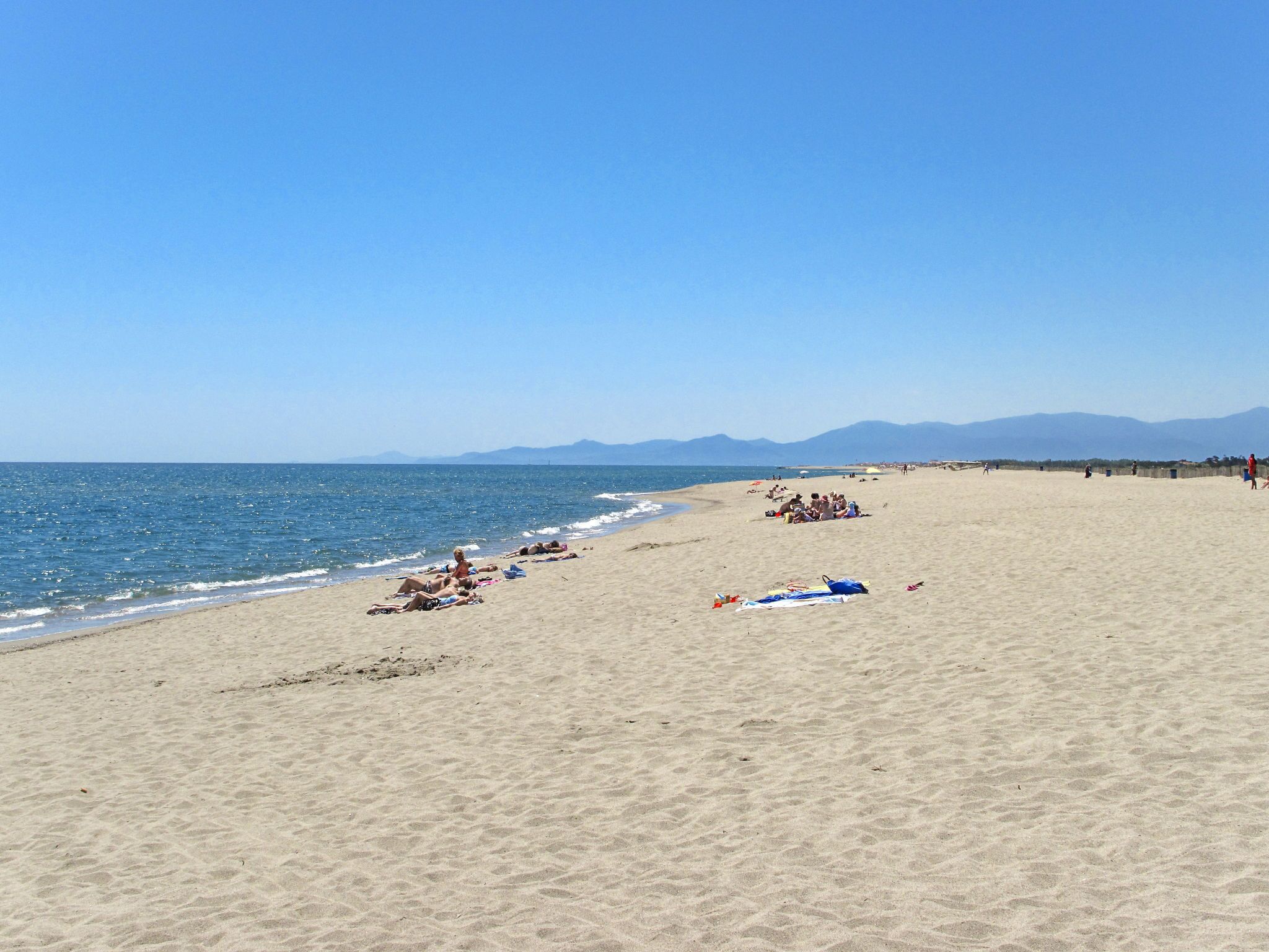 A wide sandy beach with people sunbathing and swimming.