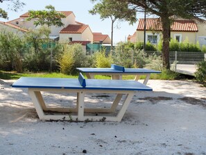 Dos mesas de picnic en una zona arenosa con edificios al fondo.