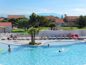 Una piscina con sillones de descanso y algunas personas.