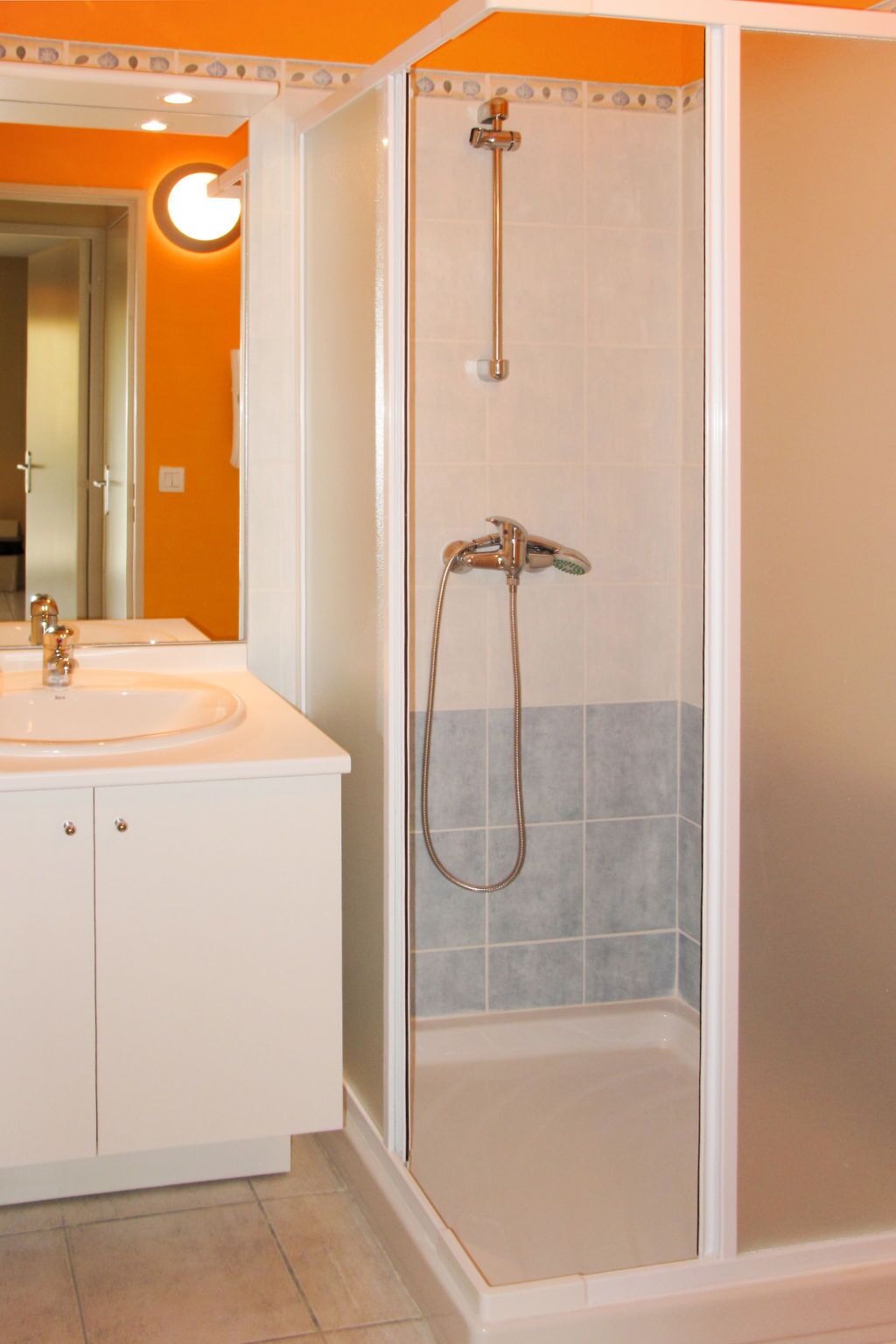Een badkamer met een douche, wastafel en spiegel.
