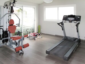 Un gimnasio en casa con cinta de correr, banco de pesas y diverso equipo de ejercicio.